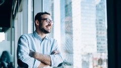 Cheerful male entrepreneur with crossed hands standing near offi